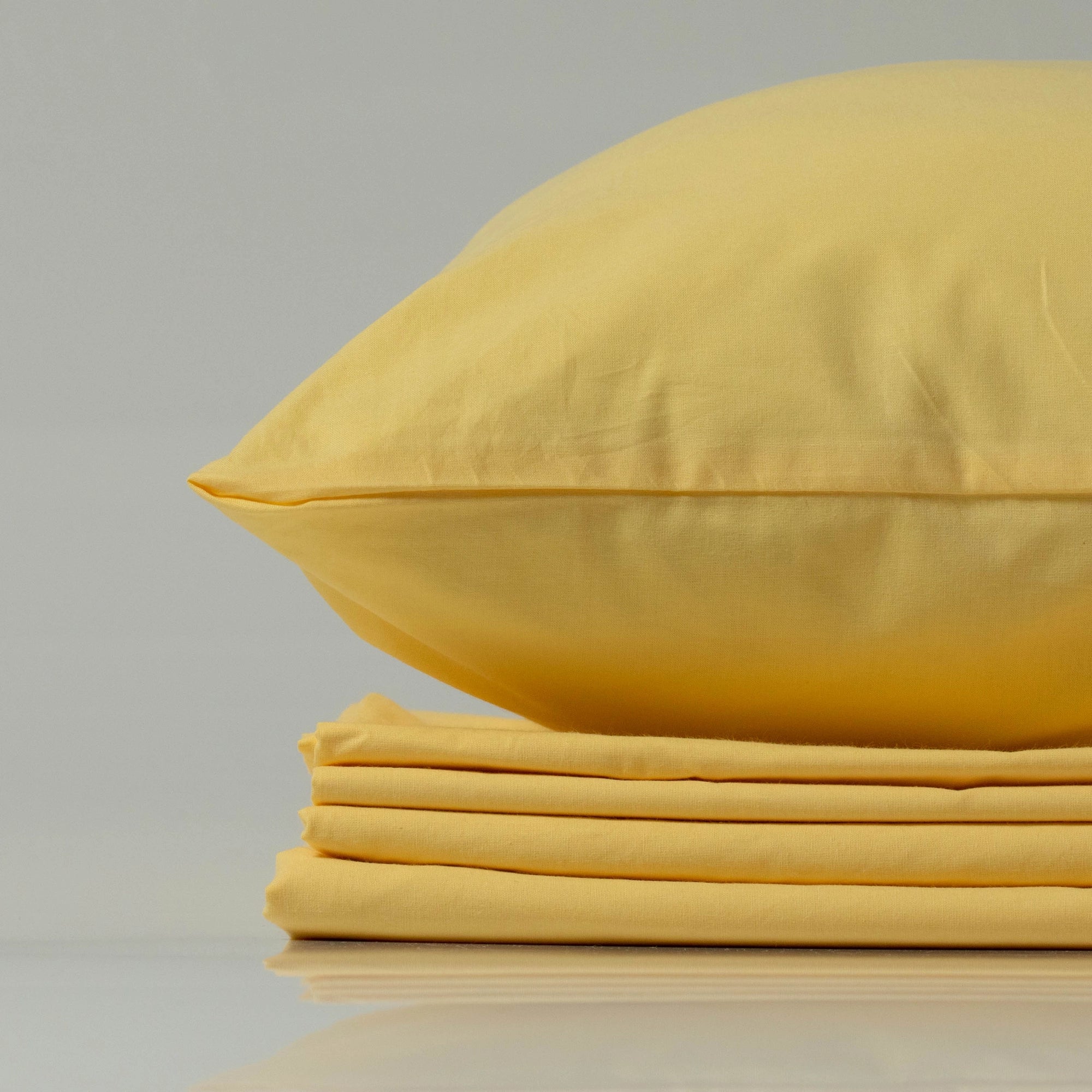 М’яка жовта наволочка з ранфорсу від Supreme Rest на акуратно складеному комплекті постільної білизни.