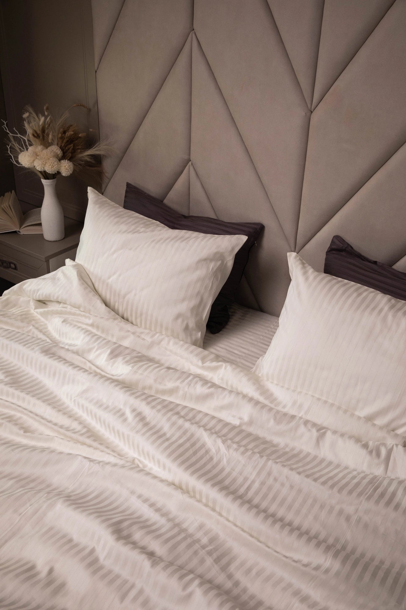 Кут ліжка з акуратно заправленою постіллю в ніжному теплом кремовому тоні.