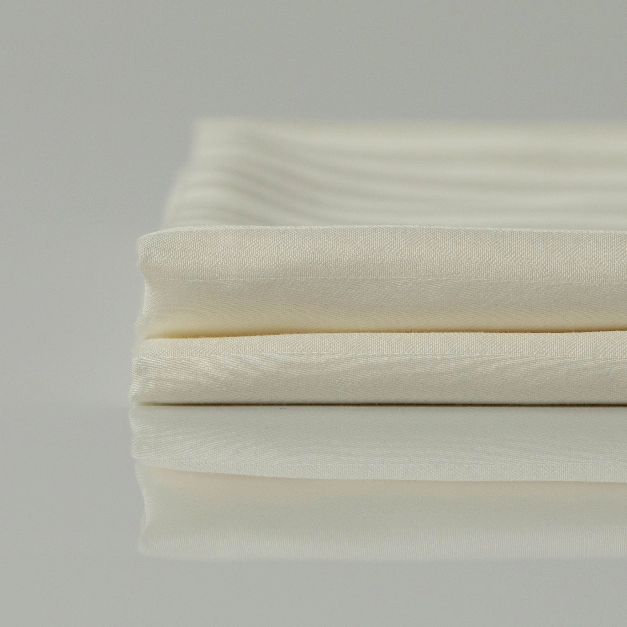 Ліжко з постіллю кольору слонової кістки в ранковому світлі - м’якість і спокій.