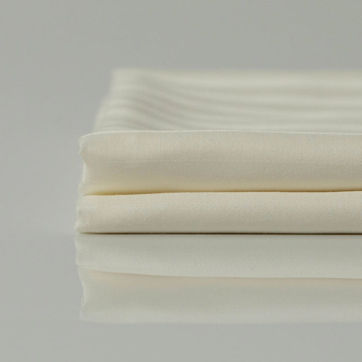 Ліжко з постіллю кольору слонової кістки в ранковому світлі - м’якість і спокій.