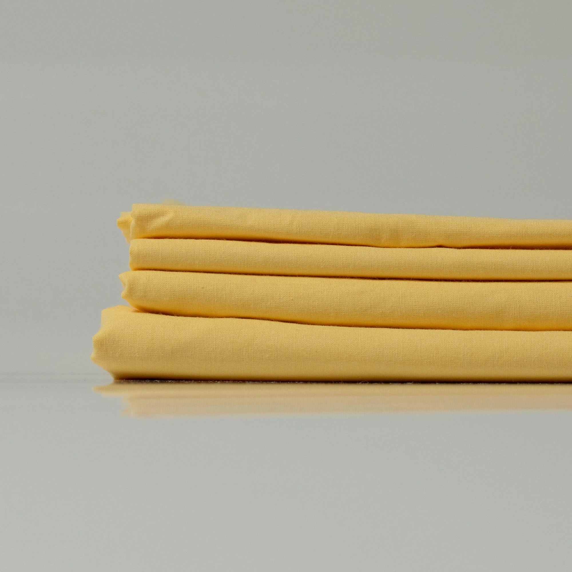 Стопка жовтих простирадл з ранфорсу (100% бавовна), що підкреслює їхню легкість і дихаючу текстуру.
