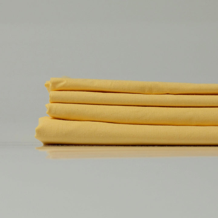 Стопка жовтих простирадл з ранфорсу (100% бавовна), що підкреслює їхню легкість і дихаючу текстуру.
