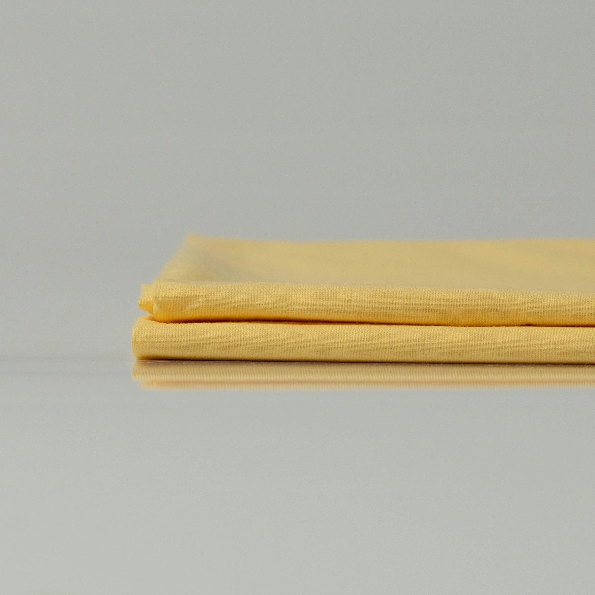 Акуратно складені яскраво жовті простирадла з ранфорсу, що демонструють гладку текстуру та дихаючу бавовняну тканину.