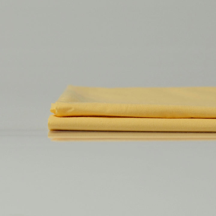 Акуратно складені яскраво жовті простирадла з ранфорсу, що демонструють гладку текстуру та дихаючу бавовняну тканину.