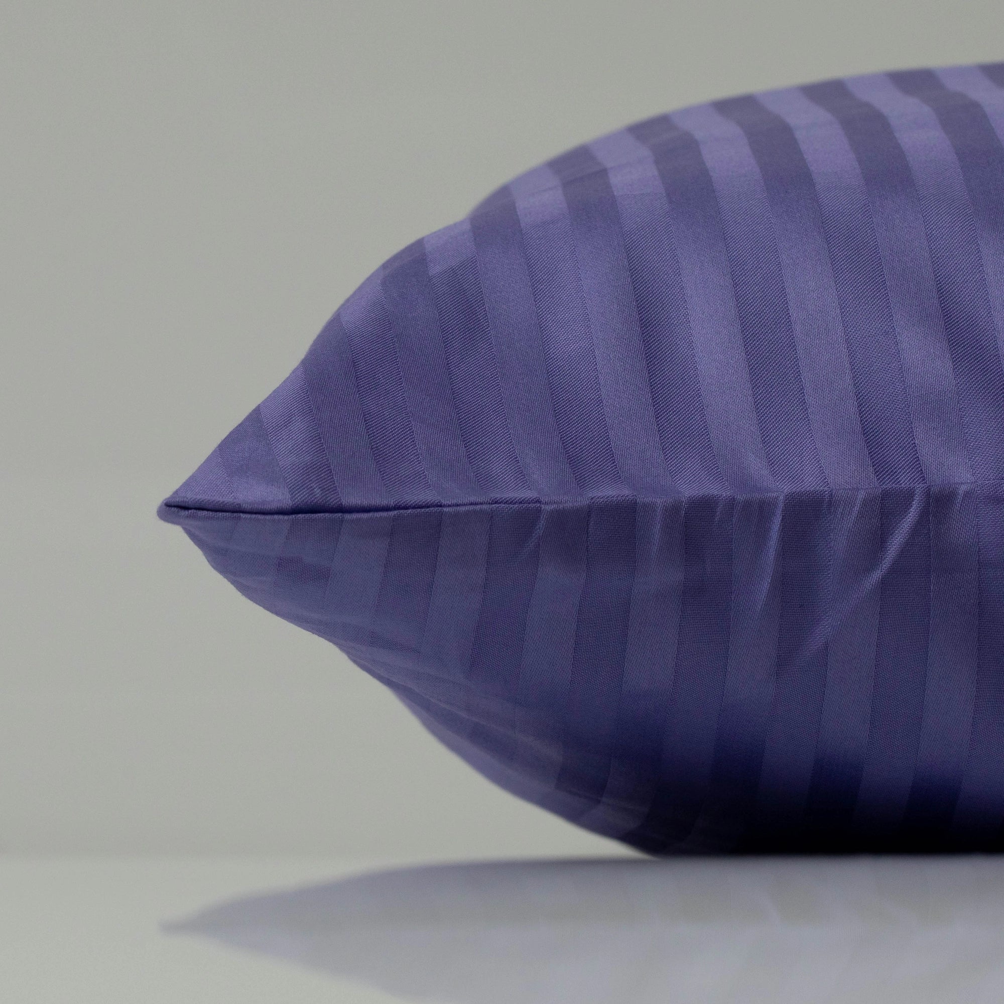 Фіолетова наволочка зі смугастим сатиновим оздобленням, що додає вишуканості ліжку.