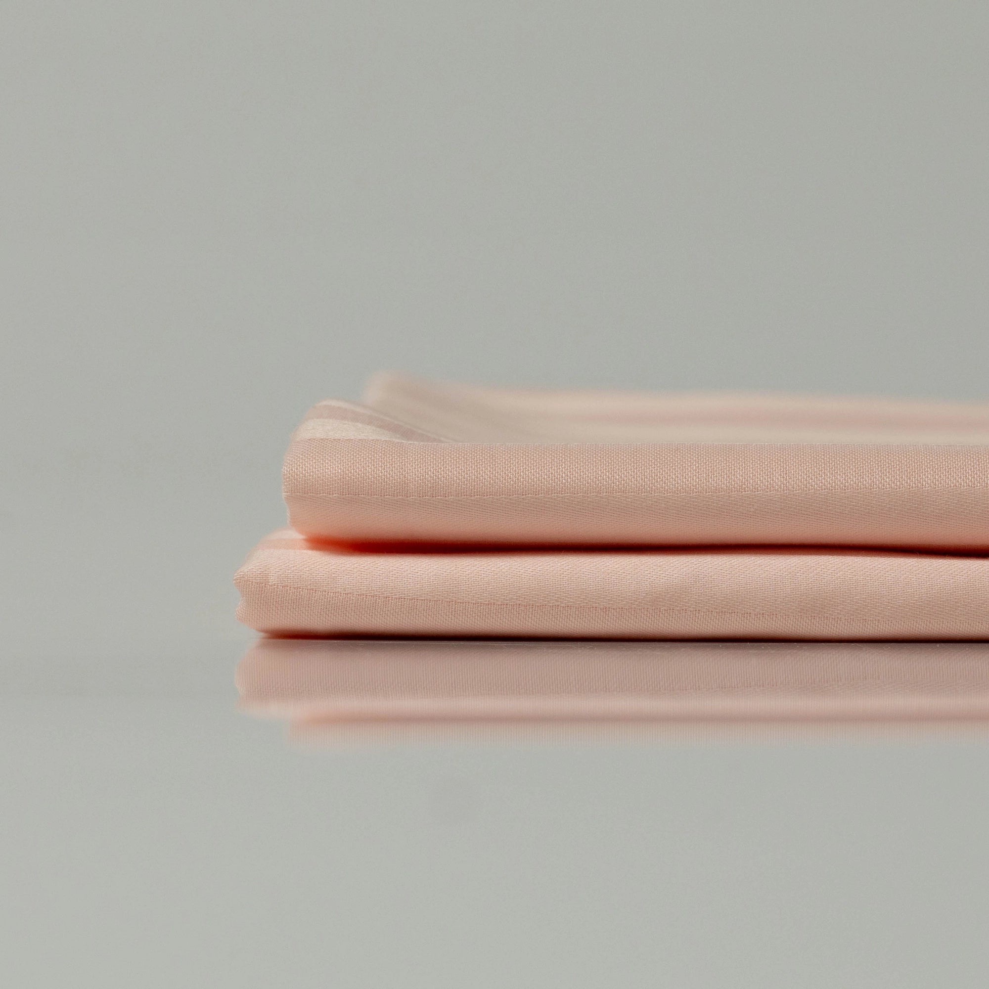 Ретельно складені простирадла ніжно-персикового кольору, що підкреслюють легку та дихаючу текстуру бавовни.
