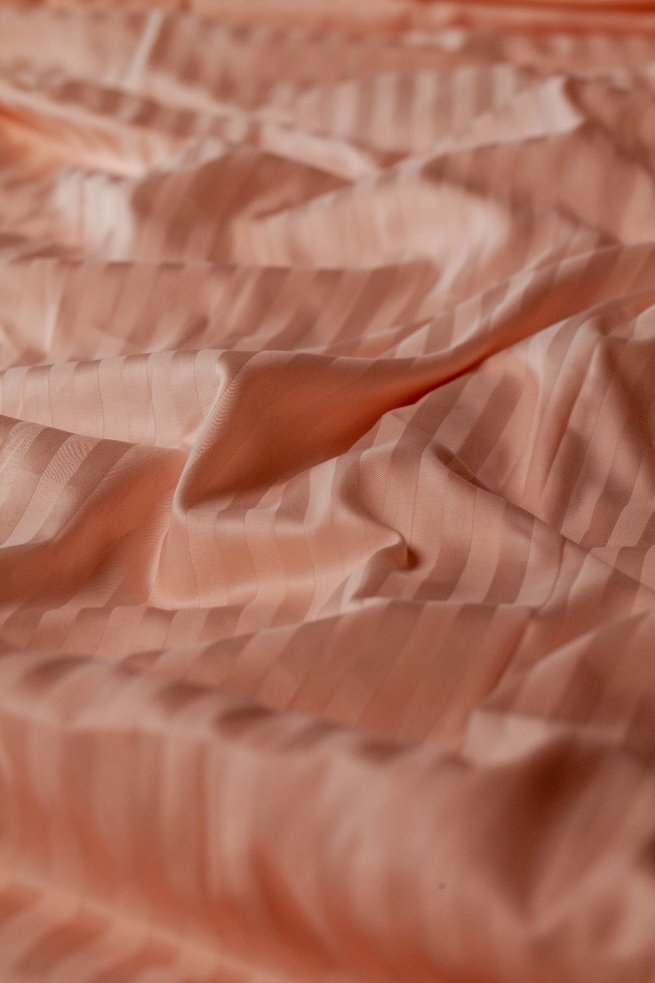 Крупний план персикової підковдри з сатину зі смугастим візерунком, що м’яко лягає природними хвилями.