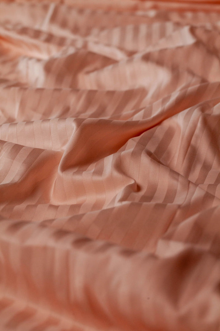 Крупний план персикової підковдри з сатину зі смугастим візерунком, що м’яко лягає природними хвилями.