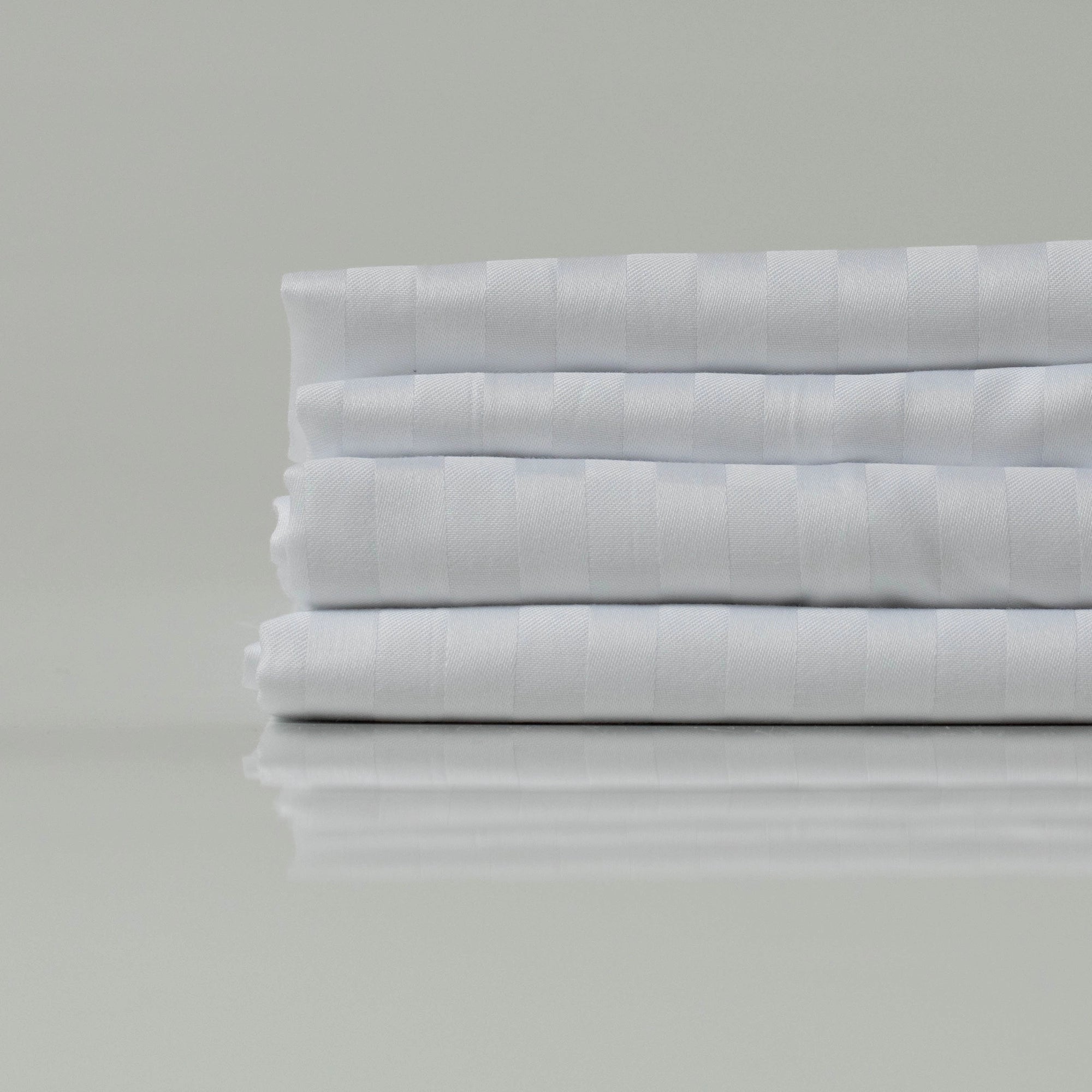 Складені білі простирадла зі страйп-сатину - гладкі, блискучі та зносостійкі, ідеальні для створення елегантної спальні.