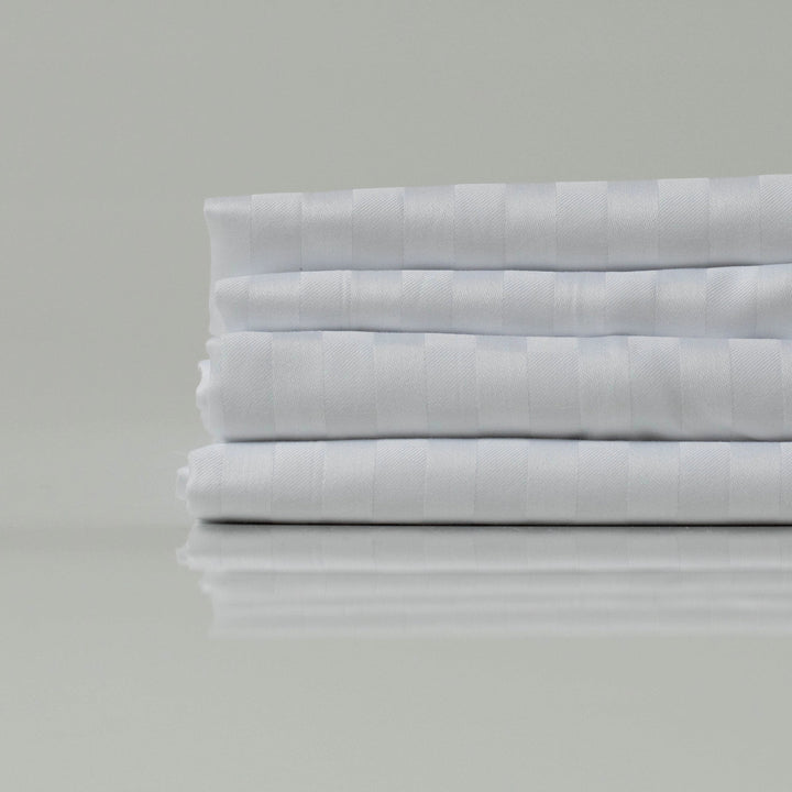 Складені білі простирадла зі страйп-сатину - гладкі, блискучі та зносостійкі, ідеальні для створення елегантної спальні.