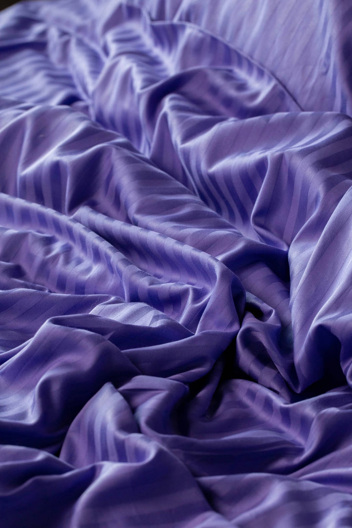 Крупний план підковдри у фіолетово-лавандових тонах з елегантним смугастим візерунком із м’якого сатину з бавовни.