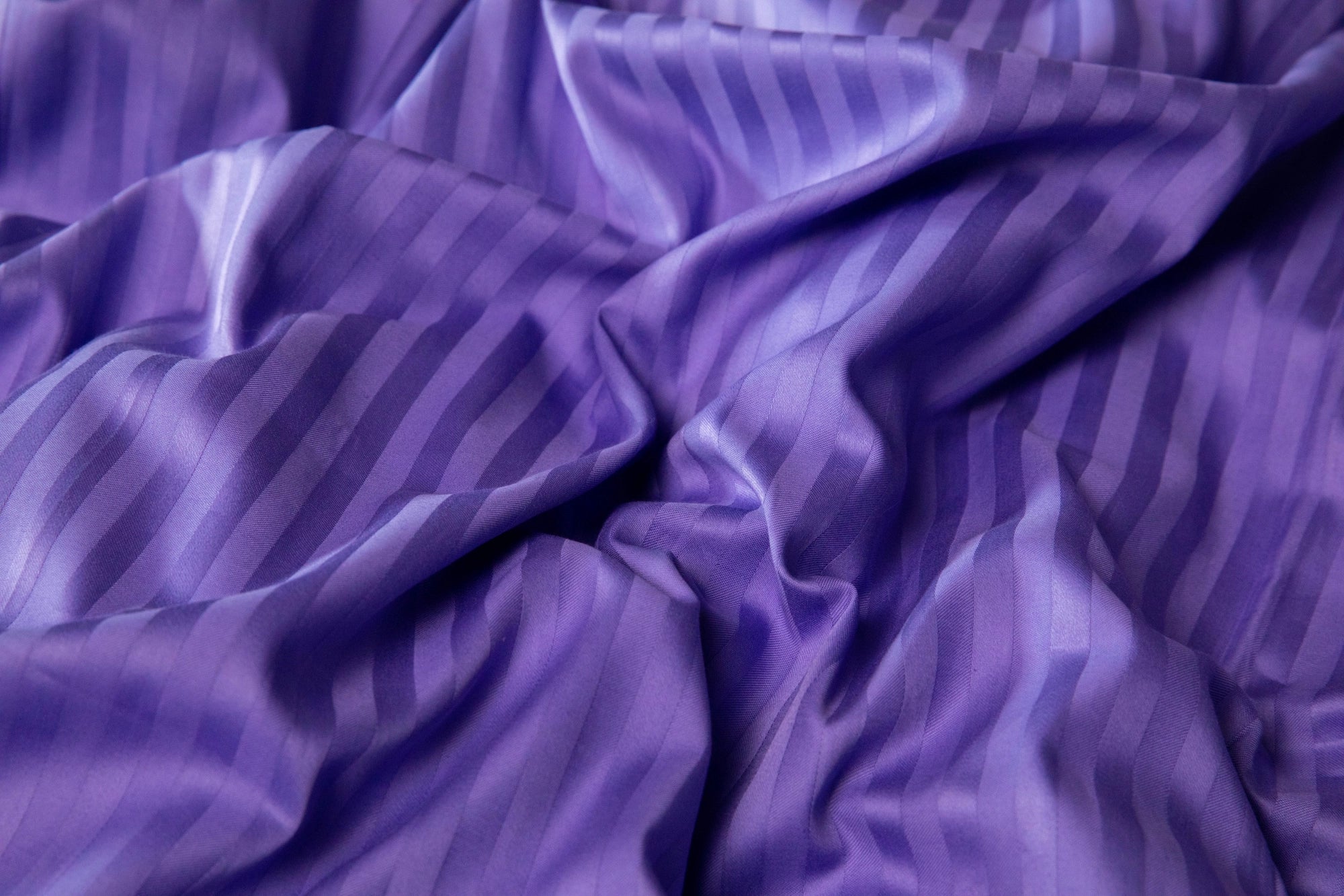 Зім’ята фіолетово-лавандова підковдра, що підкреслює м’якість і природне спадання сатинової тканини.